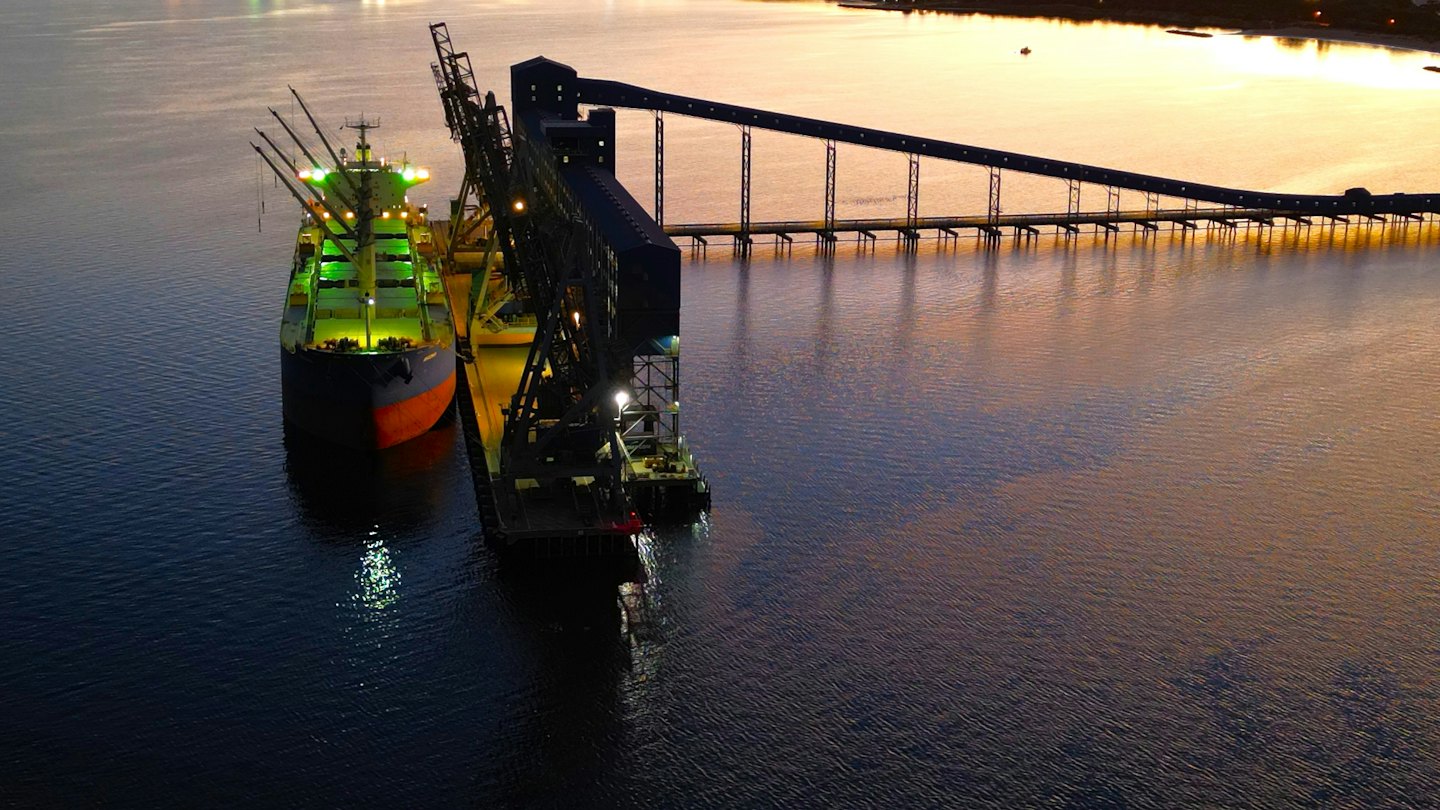 Cargo ship at industrial port with green deck lights and sunset.